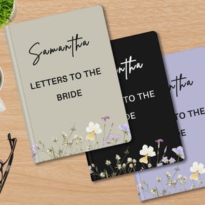 May include: Three notebooks with floral designs and the text "Samantha Letters to the Bride". The notebooks are in beige, black, and lavender. A cup of coffee, pen, glasses, and a plant are on the wooden surface.