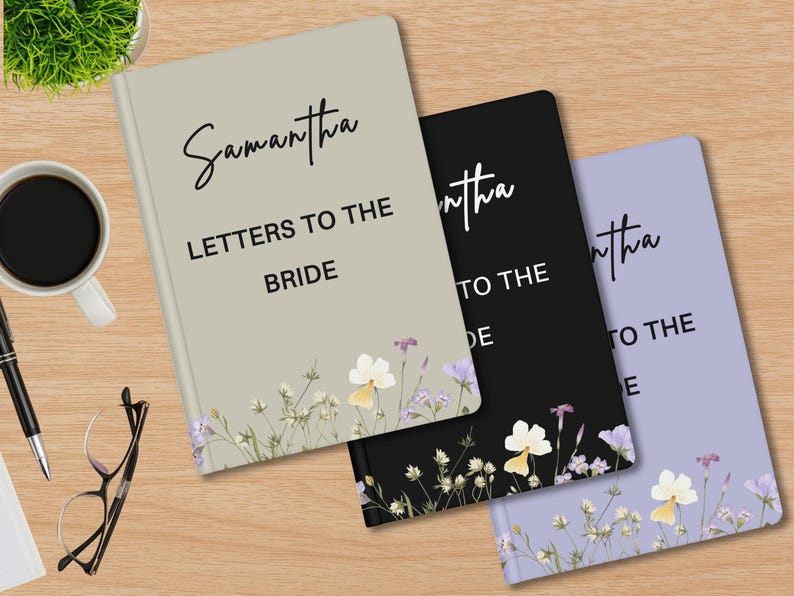 May include: Three notebooks with floral designs and the text "Samantha Letters to the Bride". The notebooks are in beige, black, and lavender. A cup of coffee, pen, glasses, and a plant are on the wooden surface.