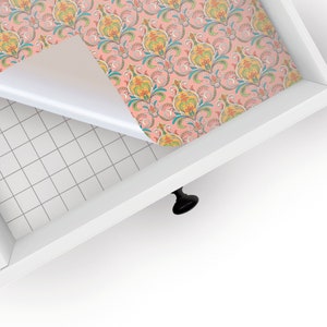 May include: A drawer liner with a pink background and a colorful paisley pattern. The liner is being peeled back to reveal the white drawer surface underneath.