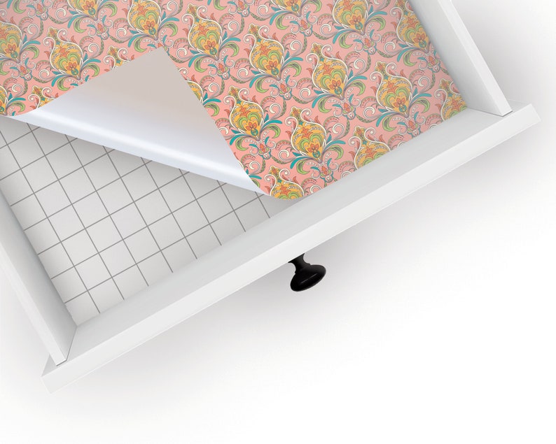 May include: A drawer liner with a pink background and a colorful paisley pattern. The liner is being peeled back to reveal the white drawer surface underneath.