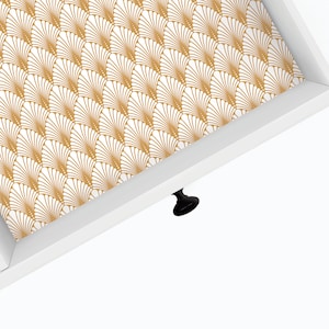 May include: White drawer with a gold and white geometric pattern lining the inside. The drawer has a black knob.