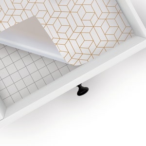 May include: A white drawer with a gold geometric patterned liner being pulled open. The liner is partially peeled back to reveal the white drawer bottom.
