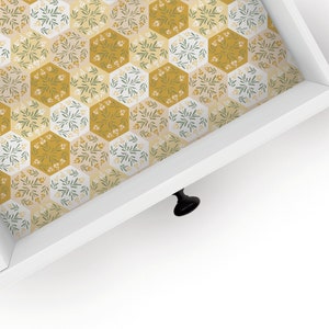 May include: White drawer with a black knob and a patterned liner. The liner is a repeating pattern of hexagonal shapes with a floral design in shades of yellow, green, and white.