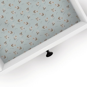 May include: A white drawer with a light blue liner featuring a repeating pattern of brown rockets. The drawer has a black knob.
