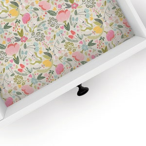 May include: A white drawer with a floral pattern lining the inside. The drawer has a black knob.