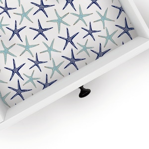 May include: A white drawer with a blue and light blue starfish pattern lining the inside. The drawer is open and the black knob is visible.