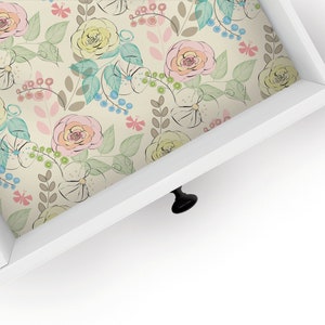 May include: A white drawer with a floral pattern liner. The drawer has a black knob.