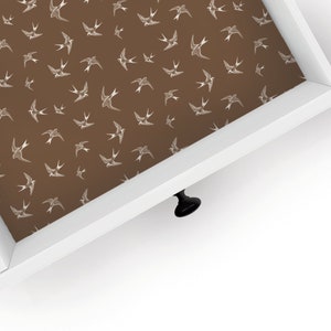 May include: A white drawer with a brown liner featuring a repeating pattern of white birds. The drawer has a black knob.