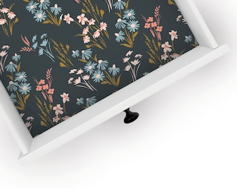May include: A white drawer with a black knob, open to reveal a dark blue liner with a floral pattern in shades of pink, blue, and gold.