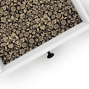 May include: A close-up of a drawer with a black and gold floral patterned liner. The drawer is white with a black knob.