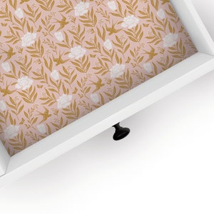 May include: A white drawer with a gold and pink floral pattern lining the inside. The drawer is open and the black knob is visible.