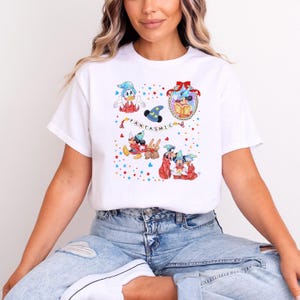 May include: White t-shirt with cartoon illustrations of Disney characters, including Mickey Mouse and Donald Duck. The word "FANTASTIC" is printed on the shirt. The shirt is worn by a person.