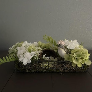 Wire basket with nest and resin bird nestled in green and white hydrangeas