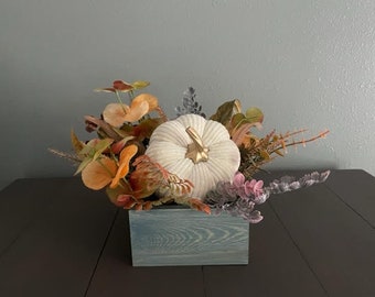 Square blue wooden planter with fabric covered foam pumpkin and arrangement of faux autumn leaves