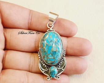 May include: A silver pendant with a large oval turquoise stone set in a silver frame. The stone has a blue and green color with gold flecks. The pendant has a silver bail for attaching to a chain.