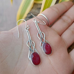 May include: A pair of silver dangle earrings with red gemstone drops. The earrings feature a delicate, intricate design with a knotted pattern.