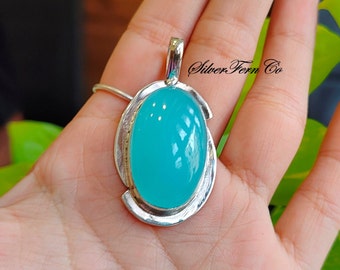 May include: A turquoise gemstone pendant with a silver setting. The pendant is oval shaped and has a smooth, polished finish. The pendant is hanging from a silver chain.