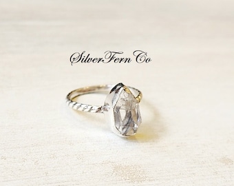 Op de afbeelding: Een zilveren ring met een heldere, peervormige edelsteen. De band is gedraaid en heeft een delicaat ontwerp. De ring is geplaatst tegen een witte achtergrond. Silver Fern Co.