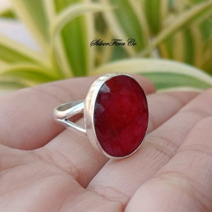 May include: A silver ring featuring a large, oval-shaped, red ruby gemstone. The ring has a simple, elegant design.