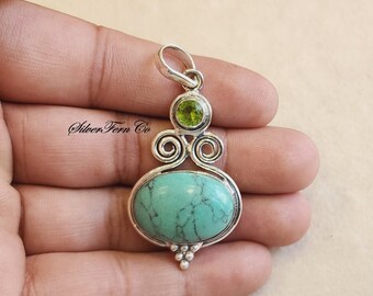 May include: Silver pendant with a turquoise stone and a green peridot stone. The pendant has a silver bail and a decorative design.