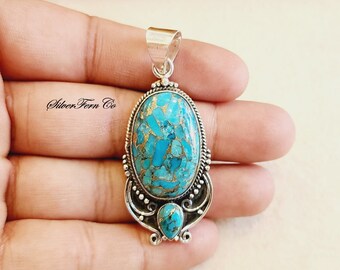 May include: Silver pendant featuring a large oval turquoise stone with gold flecks and a smaller turquoise stone at the bottom. The pendant is made of sterling silver and has a detailed design.