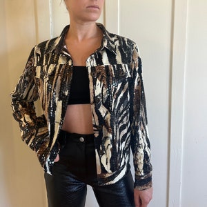 Pode incluir: Uma jaqueta de zebra preta e branca com lantejoulas. A jaqueta tem um fecho de botões e mangas compridas.