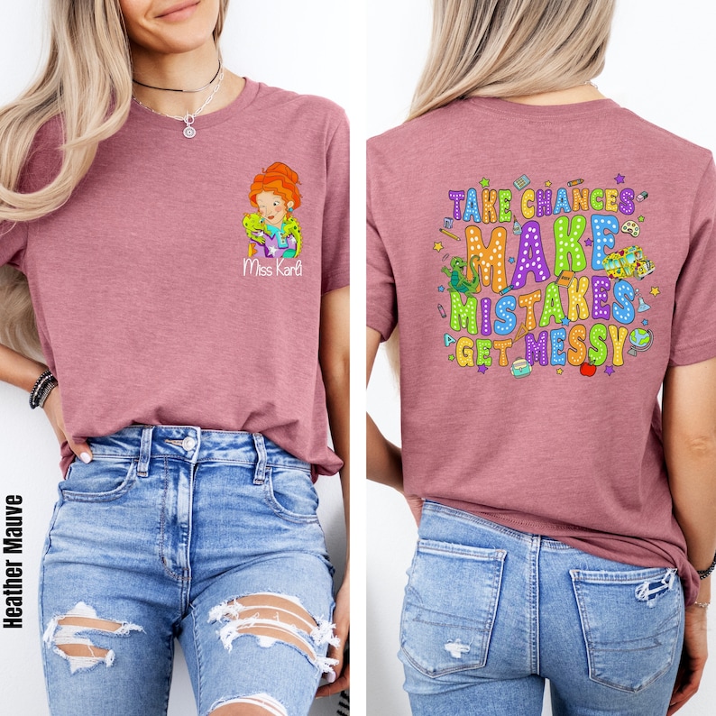 May include: A heather mauve t-shirt with a cartoon image of a teacher holding a lizard on the front and the text "Take Chances, Make Mistakes, Get Messy" on the back. The shirt is being modeled by a person wearing blue jeans.