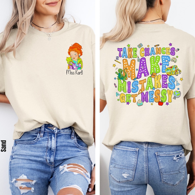 May include: A beige t-shirt with a graphic of a woman with red hair and a green lizard on the front. The back of the shirt has a colorful graphic that says "Take Chances Make Mistakes Get Messy".