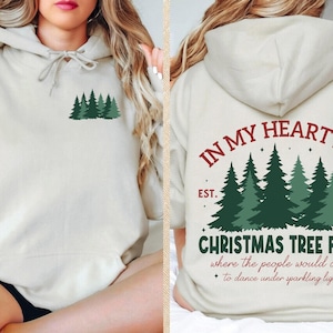 May include: Cream-colored hoodie with a forest green tree graphic on the front and back. The back of the hoodie features the text "IN MY HEART IS A CHRISTMAS TREE FARM" with the year "1989".