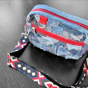May include: A small blue denim crossbody bag with red zipper accents and a black and white patterned strap.