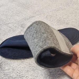 May include: A pair of gray felt insoles with a navy blue base. One insole is rolled up, revealing a light gray strap. The insoles are designed for comfort and support.