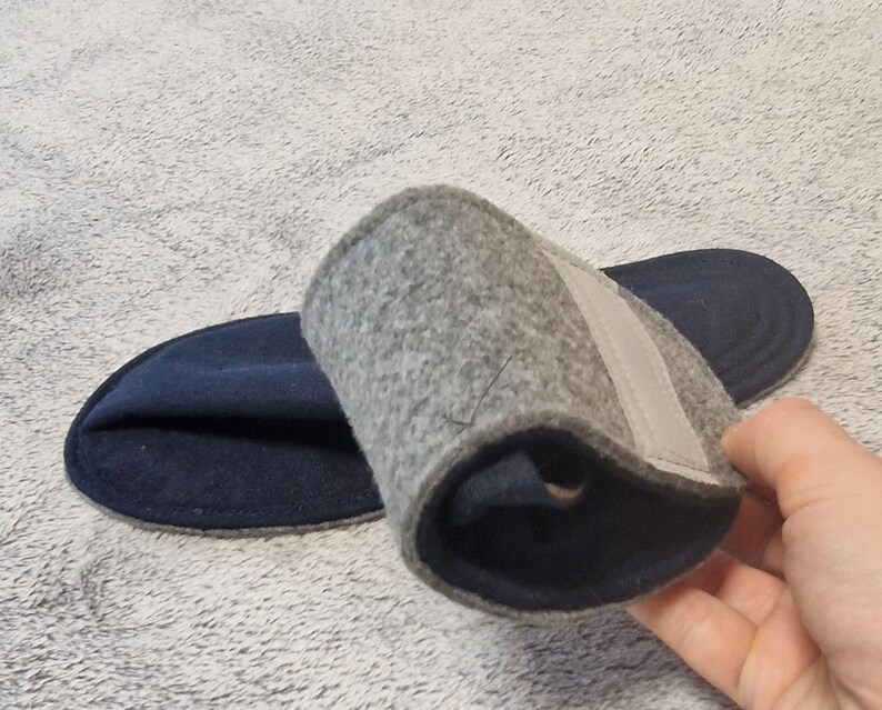 May include: A pair of gray felt insoles with a navy blue base. One insole is rolled up, revealing a light gray strap. The insoles are designed for comfort and support.