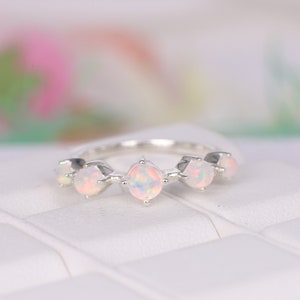 以下が含まれることがあります： 5つの丸い虹色のオパール宝石をあしらったシルバーリング。 オパールは繊細な爪のデザインでセットされており、きらびやかでエレガントなジュエリーです。 リングは柔らかくぼやけた背景に配置されています。