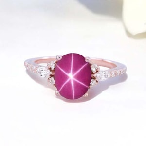 Peut inclure: Une bague en or rose avec une pierre précieuse saphir étoilé rose entourée de diamants plus petits.