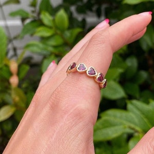 May include: A gold band ring with a row of small, heart-shaped red gemstones.