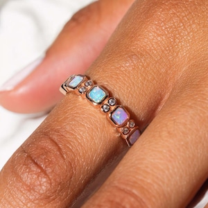 Könnte beinhalten: Ein Roségold-Bandring mit einer Reihe quadratischer Opale und kleinen klaren Edelsteinen.