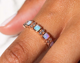 May include: A rose gold band ring with a row of square-shaped opals and small clear gemstones.
