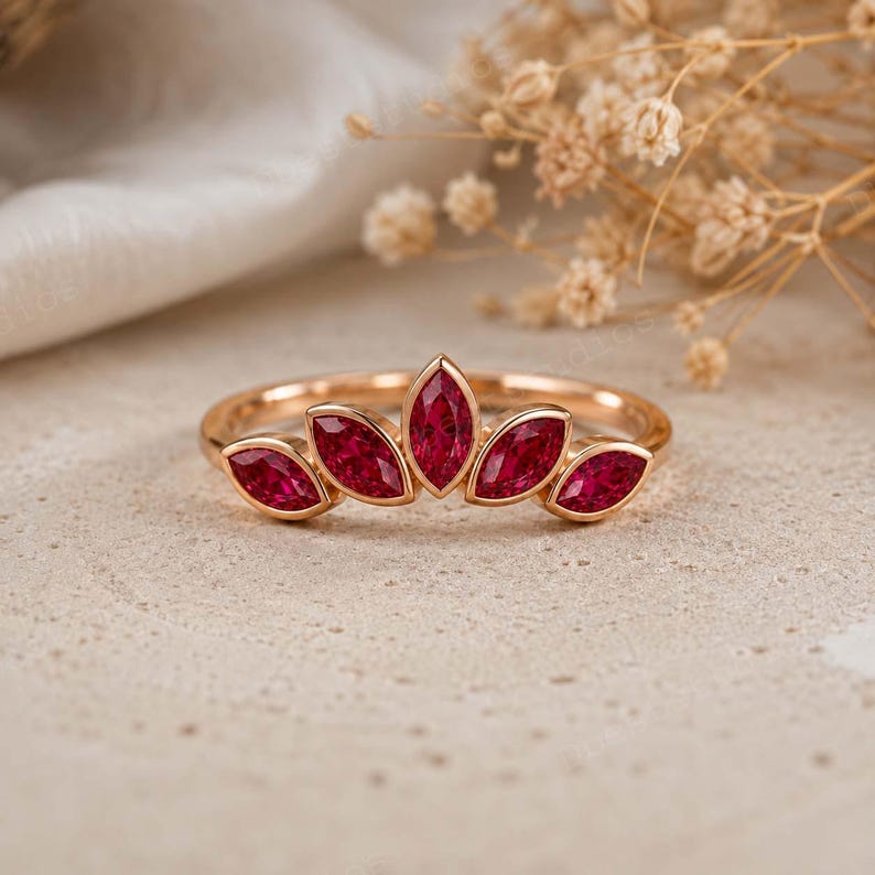 Peut inclure: Une bague en or rose orn&eacute;e de cinq pierres pr&eacute;cieuses rouges taille marquise dispos&eacute;es en forme de couronne en &eacute;ventail. L'anneau est fin et poli, avec la pierre centrale plus grande, flanqu&eacute;e de deux pierres plus petites de chaque c&ocirc;t&eacute;.