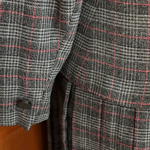 K&ouml;nnte beinhalten: Nahaufnahme eines grau-schwarz karierten Blazers mit roten Akzentlinien. Der Blazer hat eine gekn&ouml;pfte Manschette und ein ma&szlig;geschneidertes Design. Der Stoff hat ein strukturiertes Aussehen, m&ouml;glicherweise Wolle.