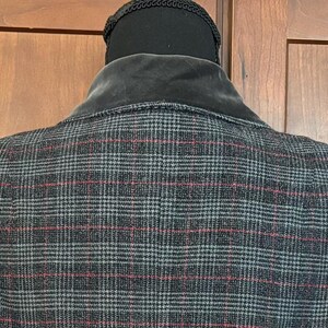 K&ouml;nnte beinhalten: Nahaufnahme der R&uuml;ckseite einer karierten Jacke. Die Jacke ist &uuml;berwiegend grau mit einem rot-blauen Karomuster. Der Kragen ist aus dunkelgrauem Samt. Die Jacke wird auf einem schwarzen Mannequinkopf pr&auml;sentiert.