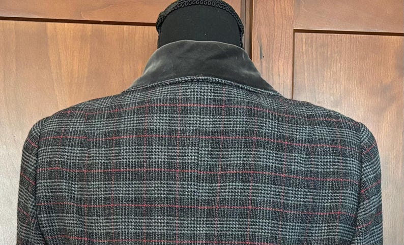 K&ouml;nnte beinhalten: Nahaufnahme der R&uuml;ckseite einer karierten Jacke. Die Jacke ist &uuml;berwiegend grau mit einem rot-blauen Karomuster. Der Kragen ist aus dunkelgrauem Samt. Die Jacke wird auf einem schwarzen Mannequinkopf pr&auml;sentiert.