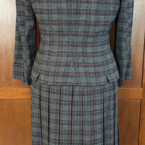 K&ouml;nnte beinhalten: Ein grauer karierter Hosenanzug mit einem Faltenrock. Die Jacke hat einen Samtkragen und der Anzug hat ein rot-blaues Karomuster. Der Anzug wird auf einer Schaufensterpuppe pr&auml;sentiert.