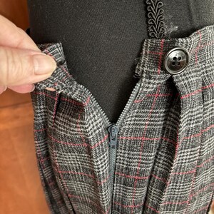 K&ouml;nnte beinhalten: Nahaufnahme eines grau karierten Rocks mit roten Akzentlinien. Der Rock hat einen Rei&szlig;verschluss und einen Knopf. Der Stoff ist &uuml;ber einer schwarzen Mannequin-Form drapiert.