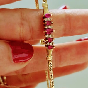 May include: A gold chain bracelet with a row of red ruby and white diamond stones.