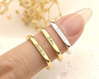 May include: Three personalized rings in gold and silver are displayed. The rings are engraved with the names "Monty", "Sophia", and "Rebecca". The rings are simple bands, perfect for everyday wear.