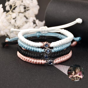 May include: Four friendship bracelets with a small, clear, round charm with a blue center. The bracelets are white, light blue, black, and pink.