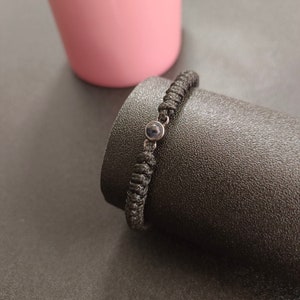 May include: A black braided bracelet with a small, round, dark blue stone charm.