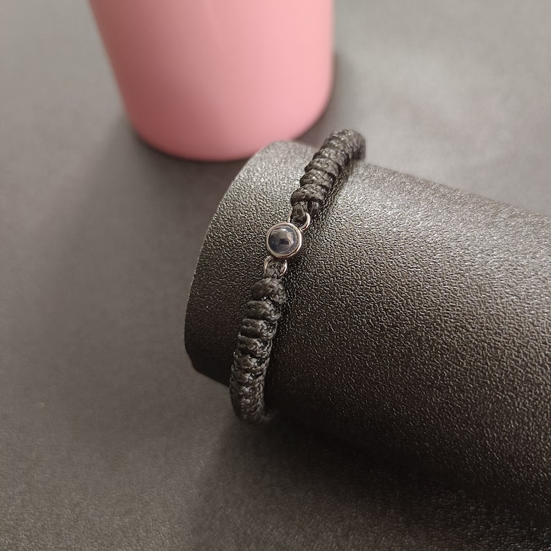 May include: A black braided bracelet with a small, round, dark blue stone charm.