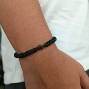 May include: A black braided bracelet with a small black bead in the center.