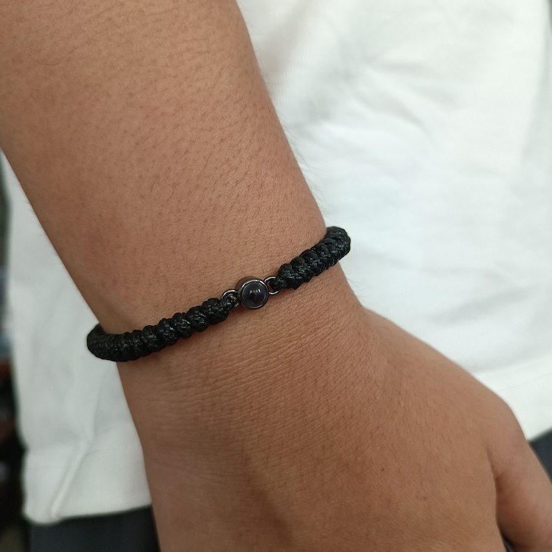 May include: A black braided bracelet with a small black bead in the center.
